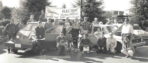 Group of peope standing with cars (including a CitCar) in front of the Electric Auto Association North Bay Chapter banner.