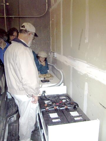 People looking down on a bank of batteries in stacked boxes.