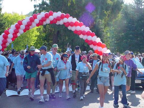 People in matching blue shirts siling and walking through red and white–striped balloon arch.